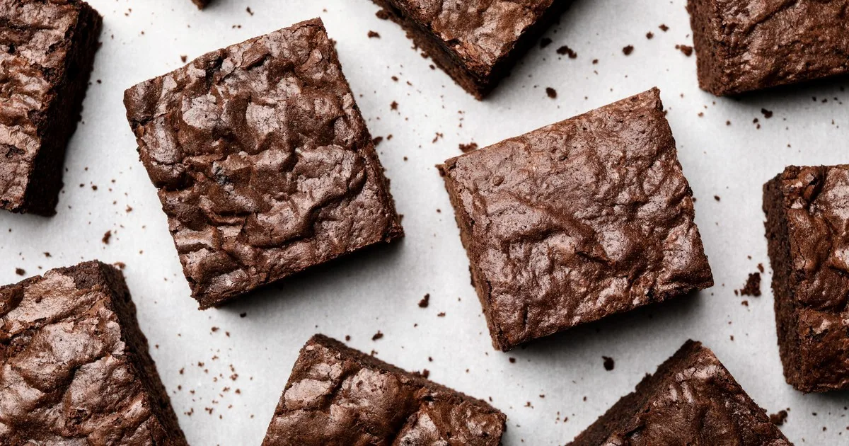Brownies de cacao cortados en cuadrados sobre papel pergamino con textura húmeda y capa crocante